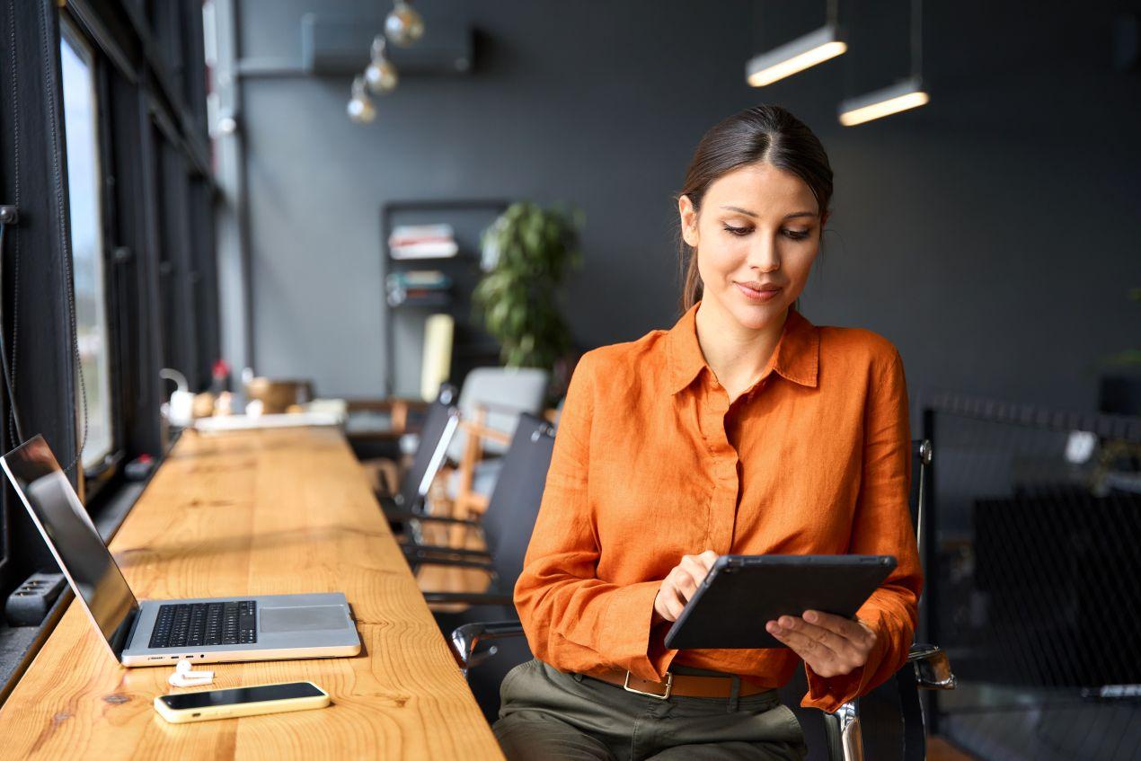 Frau nutzt Spesen App mobil im Coworking Space mit Tablet und Laptop