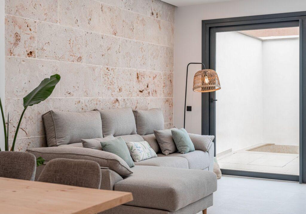 Helles Wohnzimmer mit Couch und großformatiger Steinwand aus Naturstein – zeigt haptische Wirkung strukturierter Flächen im Wohnbereich